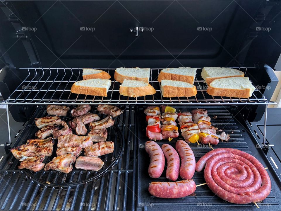 barbecue set up for grill, with ribs, sausages, skewers and bread