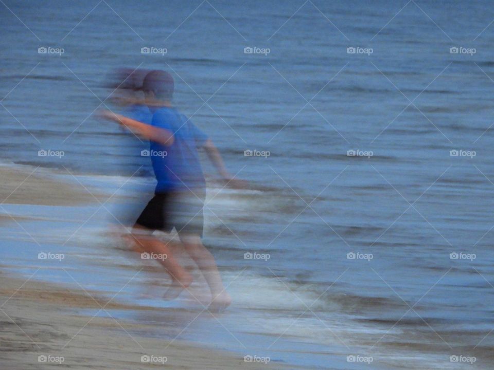 Life in Motion - A blur of a young, active boy is in motion as he runs to and from the water 