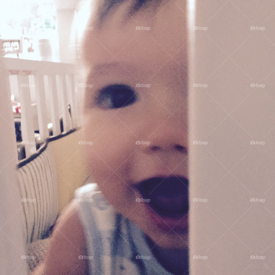 Baby boy playing peekaboo through the crib slats,smiling. 