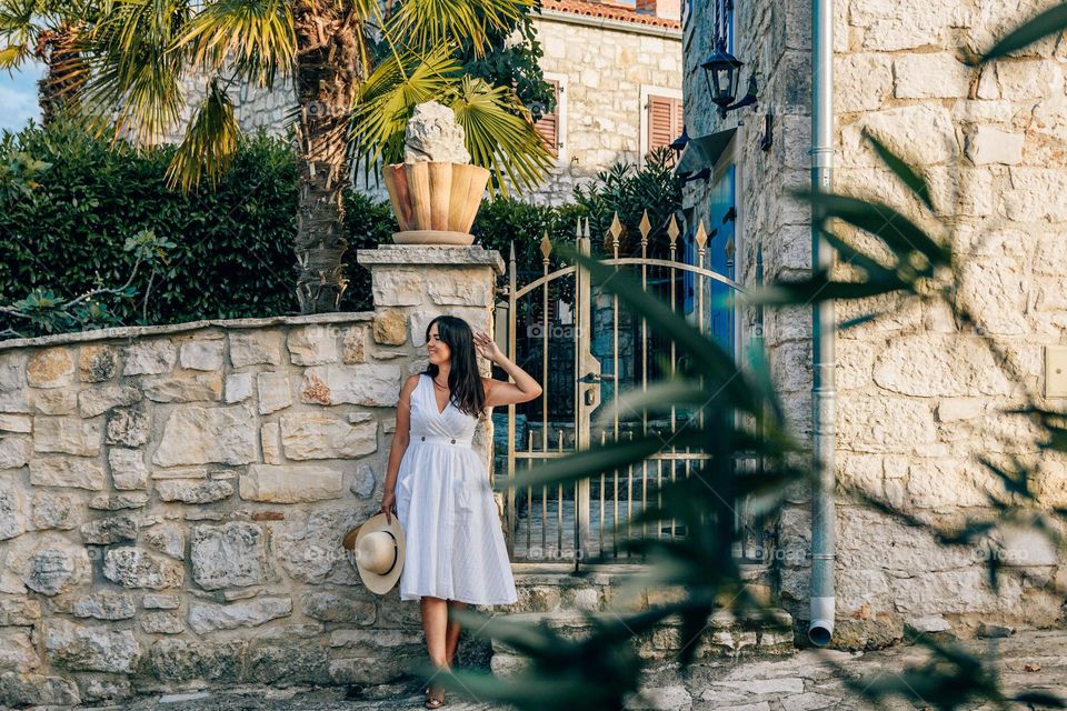 Young woman standing in front of entrance to a stone house with beautiful palm trees