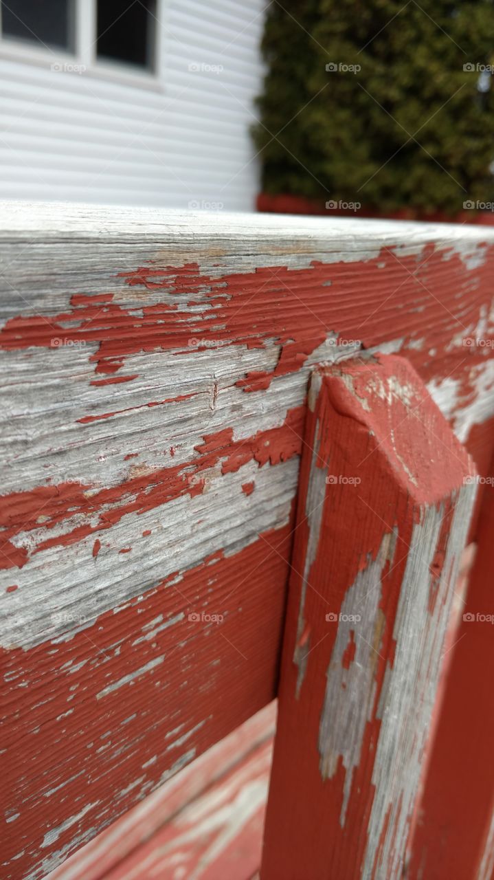 Peeling red paint on the railing of an old deck