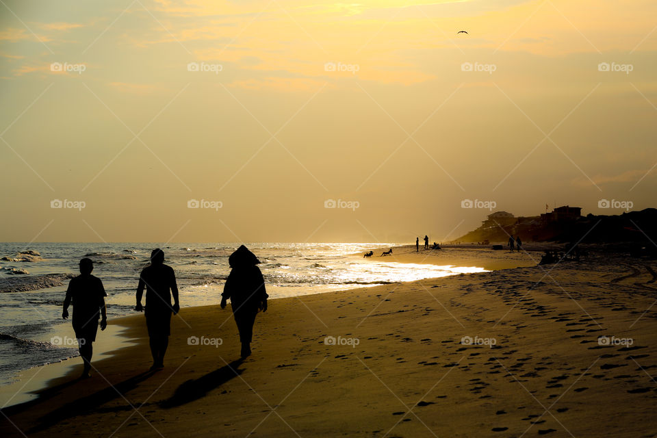 People walking on Miami Beach sunset while some others fishing at the background. 