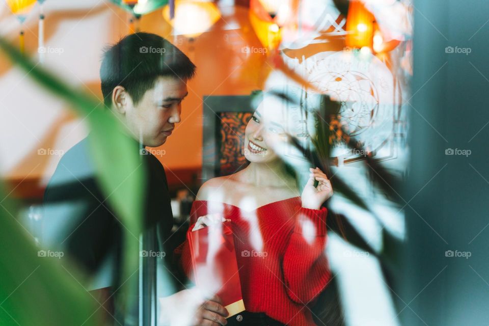 Beautiful young asian couple in red clothes give present in festive chinese vietnamese restaurant colorful paper lanterns, celebrating Chinese New Year