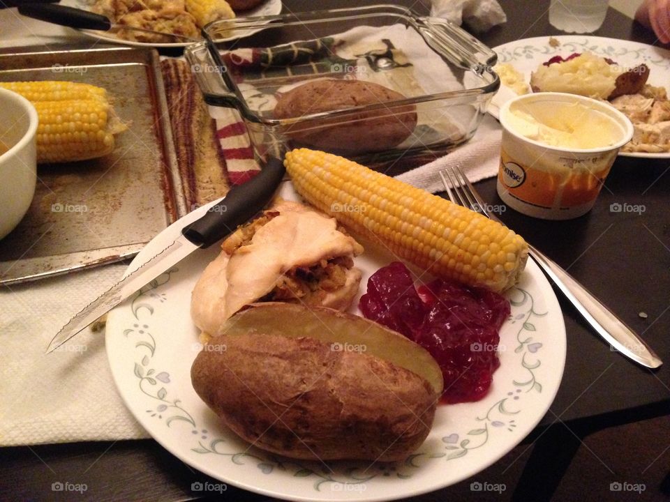 Baked potato, corn on the cob, and meat plate at dinner table 