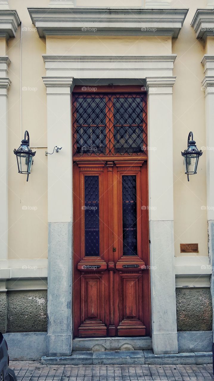 closed brown vintage wooden door on neoclassical building with couple lanterns somewhere in Athens, Greece