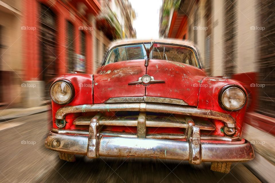Red car racing in Havana, Cuba. Classic American car in Havana, Cuba with appearance of speeding in the narrow street and matching color buildings.