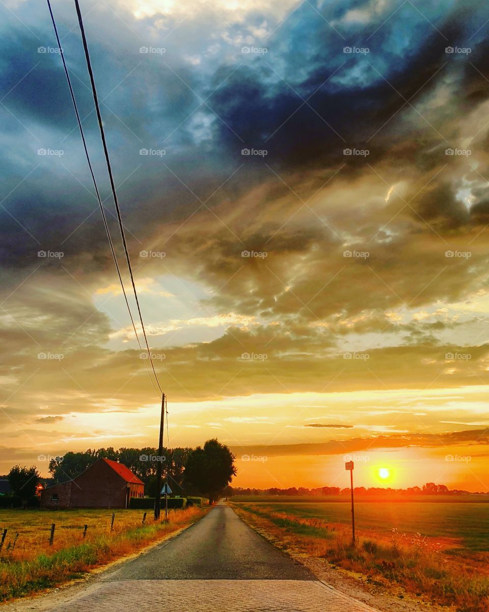 Countryside sunrise landscape with electricity lines running along a rural road passing by a farm