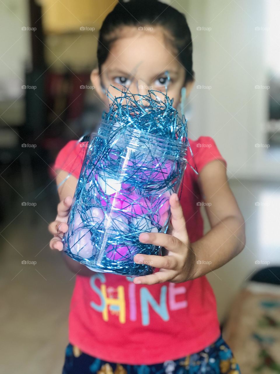 A four year old girl holds a container full of pop up balls and glitter strips.