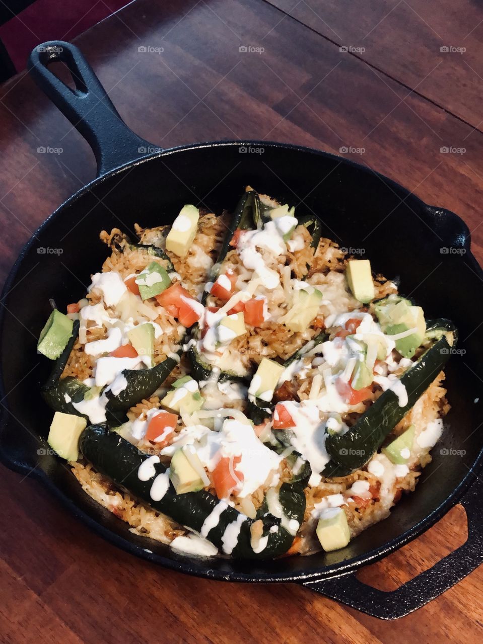 Delicious stuffed peppers with tomatoes, onions, rice, and avocado topped with a lime creme sauce baked in a cast iron pan. 