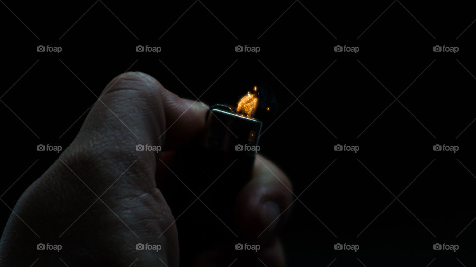 A person has lighters in his hands and he lights it through a flint wheel, the lighter ignites, sparks and fire appear, close-up on a black background.