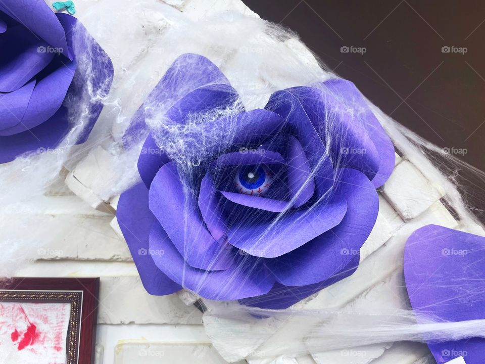 A purple flower made construction paper. It is draped in cobwebs and, in the middle, is an eyeball. 