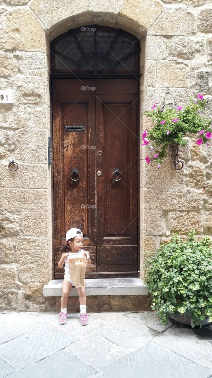 A beautiful small kid, girl waiting at the wooden door with paper bag, the doll in the bag.