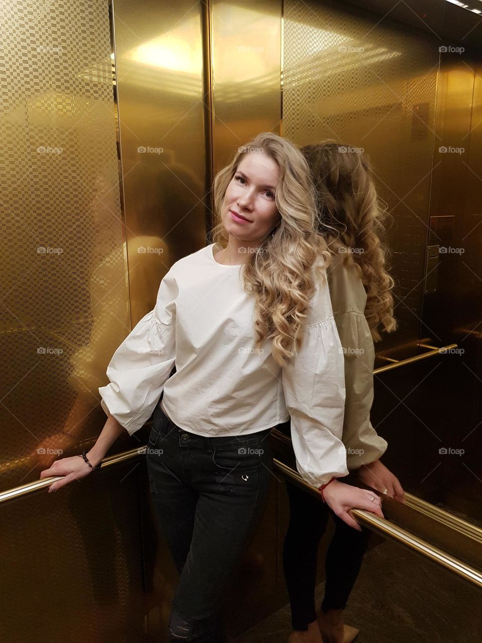 Portrait of girl with beautiful long blonde hair; she is reflected in gold-colored walls