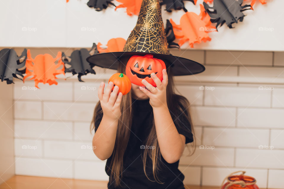 Little girl dressed as a witch for halloween holding a pumpkin with a face on the background decor