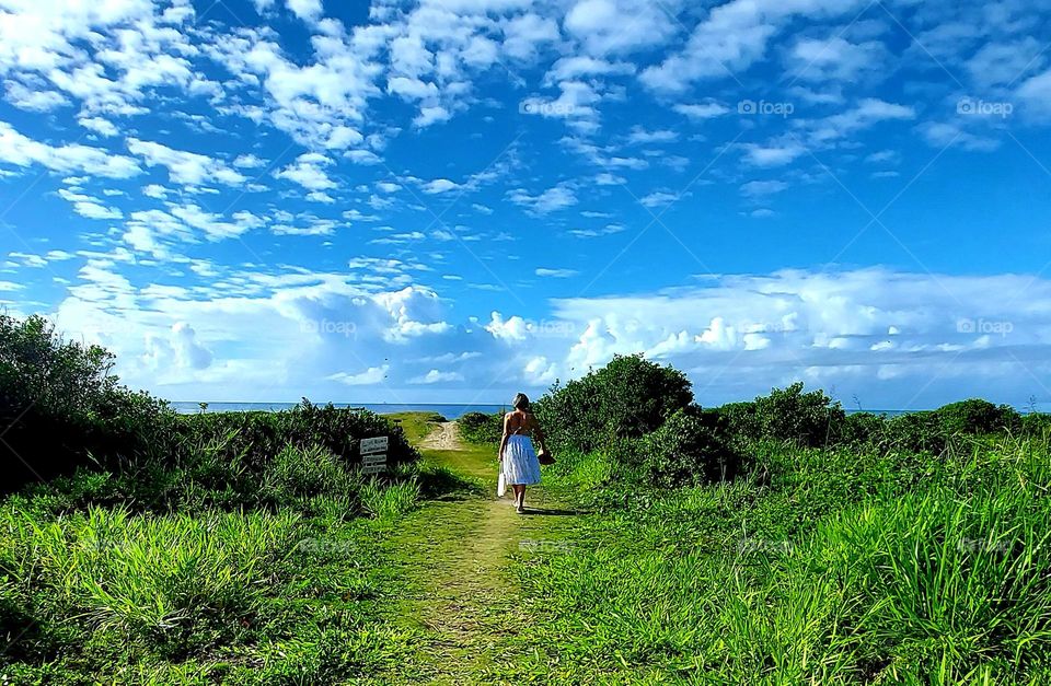 Contato com a natureza é  a garantia dr qualidade de vida. Um lindo dia de sol pede um passeio à praia, assim a mulher caminha tranquilamente para contemplar toda beleza de uma praia tranquila.