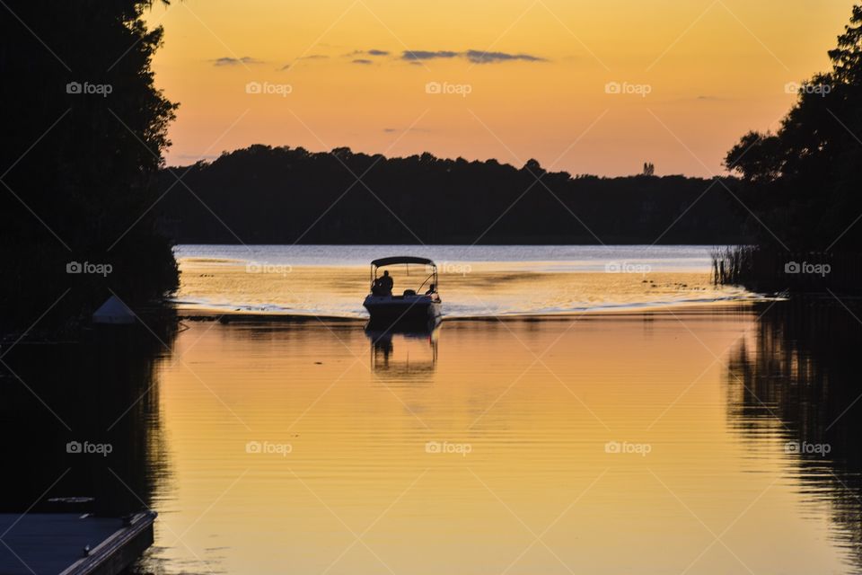 A boat returns to the lake shore at sunset. The orange sky reflects in the lake.