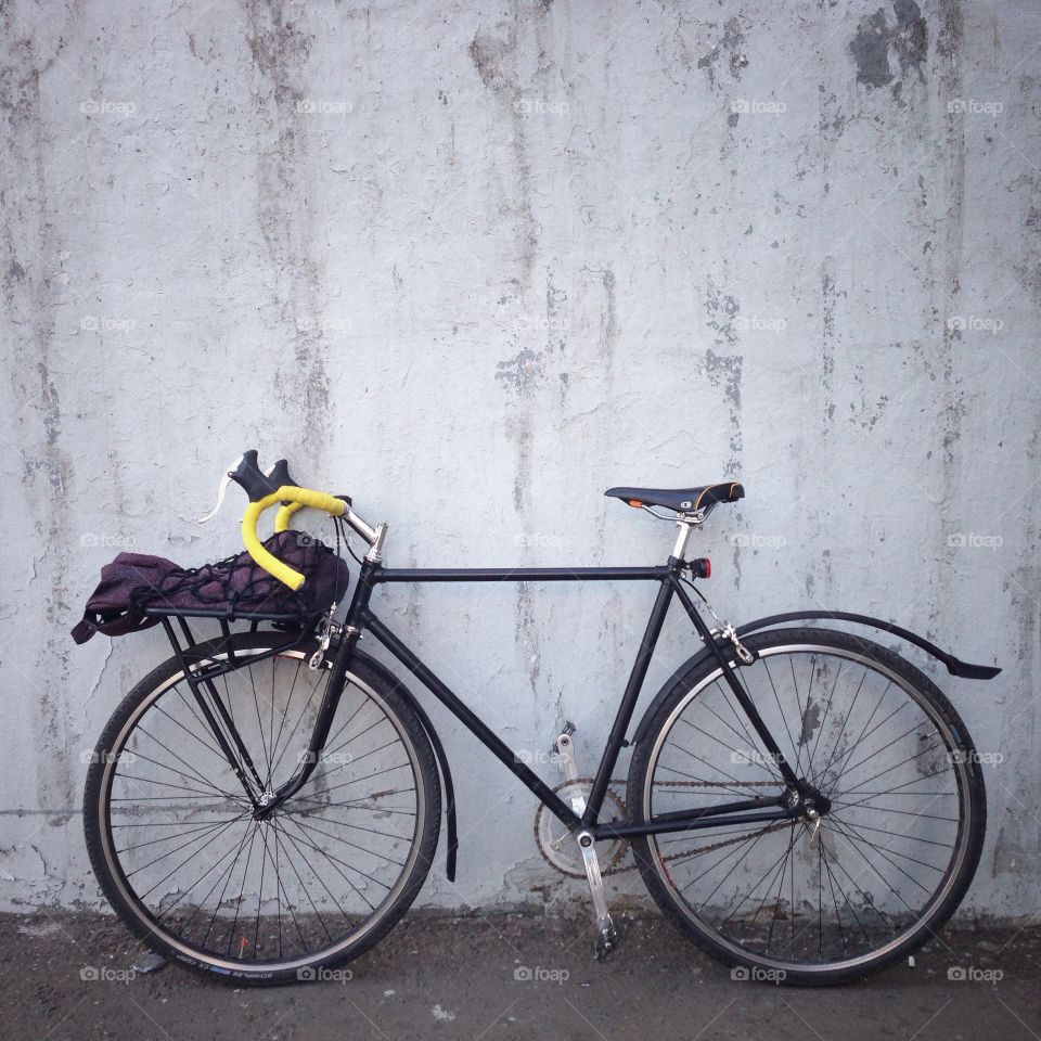 Black singlespeed soviet commuter bicycle with a front bicycle rack and yellow handlebar tape in front of white wall in Moscow, Russia