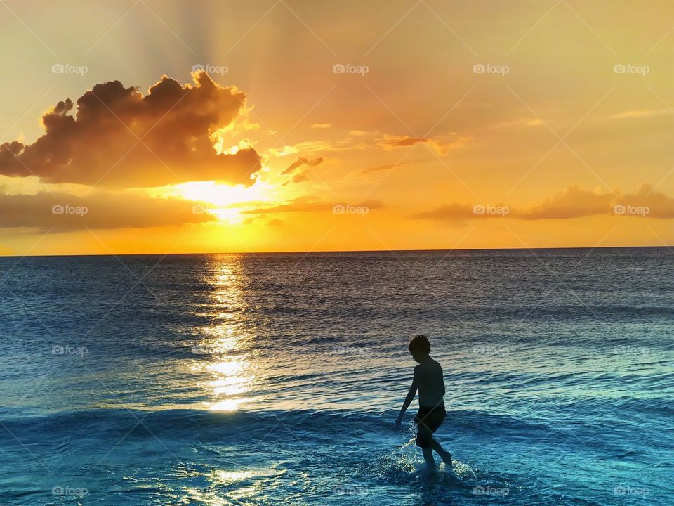 Young boy in a gorgeous blue ocean with a spectacular golden sunset reflection.