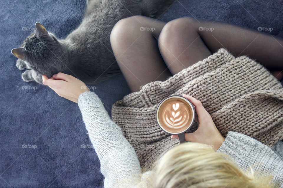 Girl with a cat and a cup of coffee resting on a bed in the room