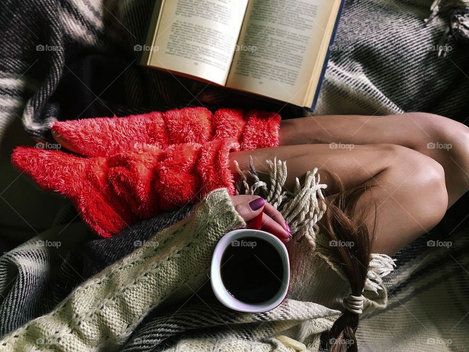 Overheard view of a home relaxing at cozy bed with warm blanket, coffee cup and favorite book 