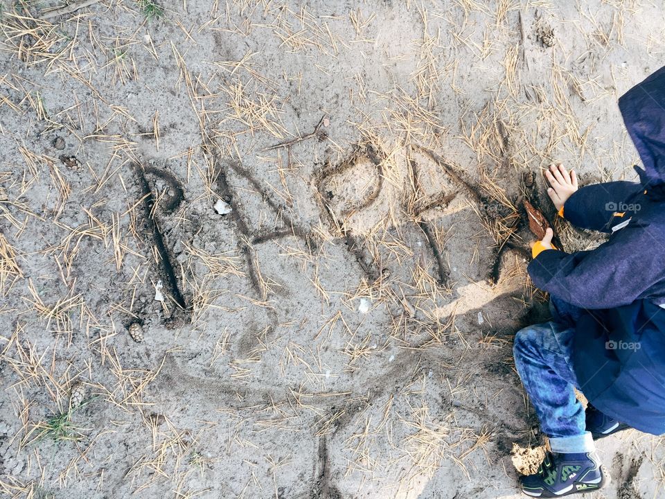 Boy writing with stick in sand. Young boy writing Papa with a stick into the sand