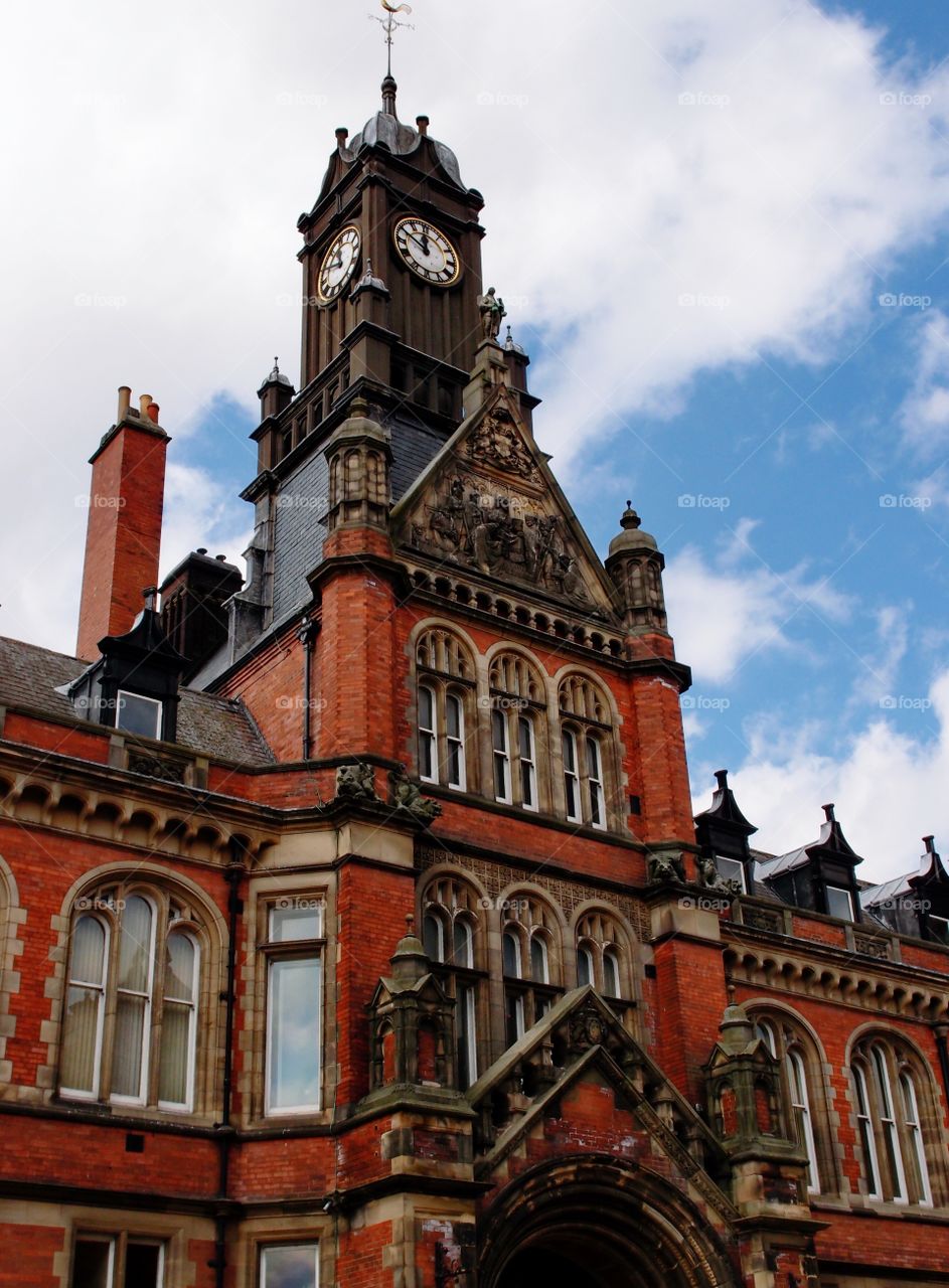 A beautiful intricately designed old brick building with lots of windows and a clock tower on a nice summer day in England. 