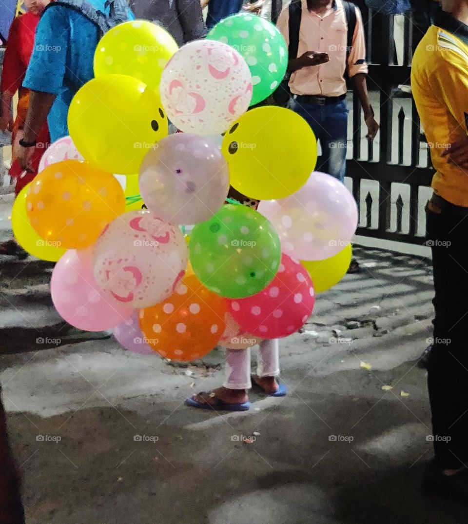 tiny hands that should play with balloons are selling balloons on the street