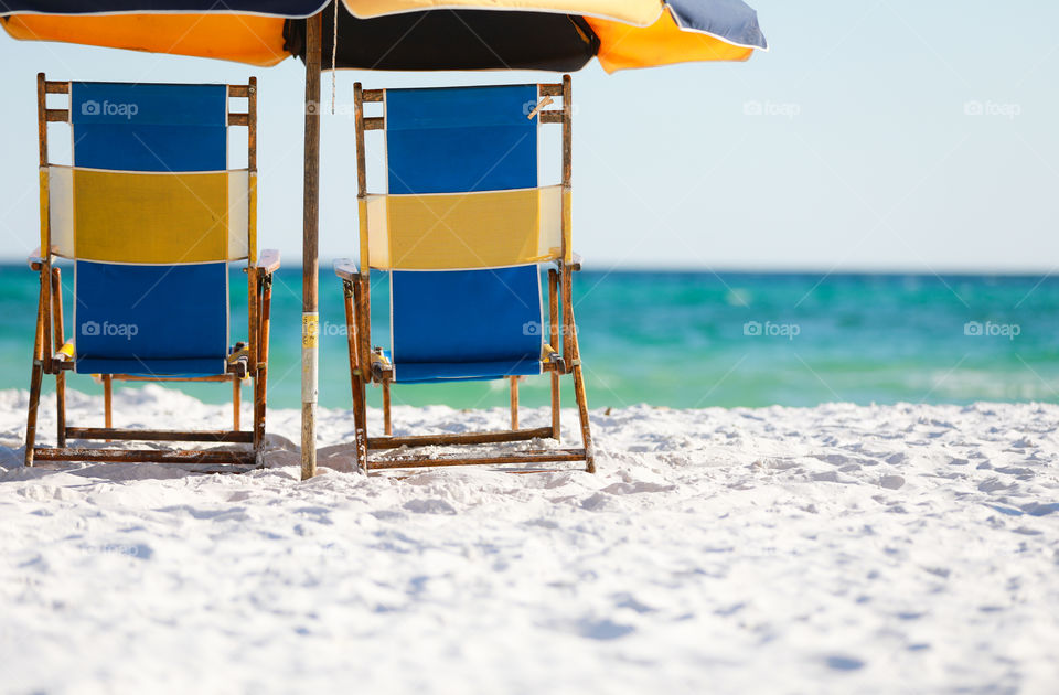 Beach chairs and umbrella sitting at a ocean front on sugar white sand in Florida