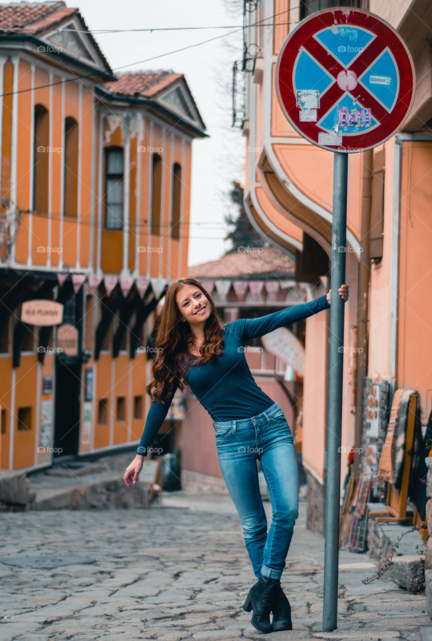 Girl smiling and holding onto a sign pole.