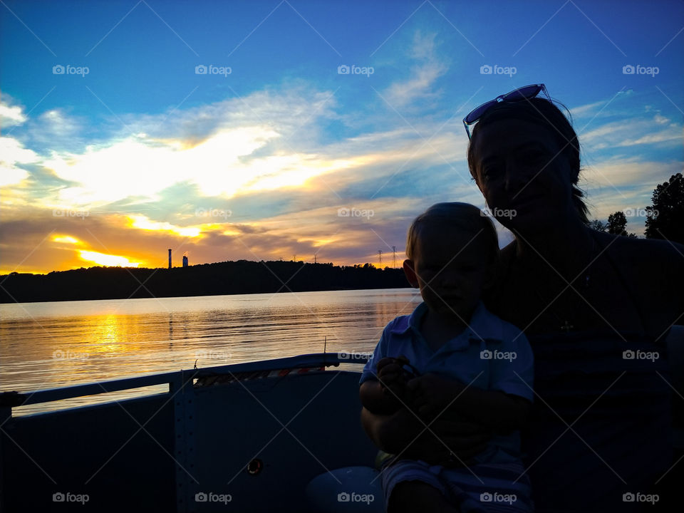 Sihouette of mother and Son sitting on boat with the sunset behind them and it reflecting off off lake water.