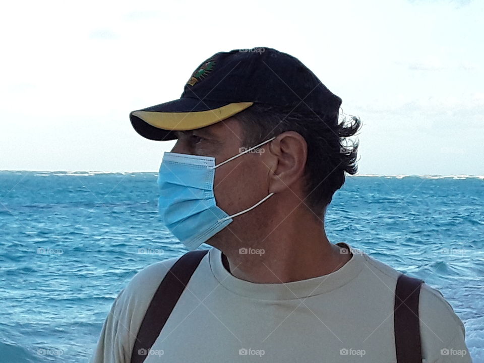 tourist in mask and cap by the ocean