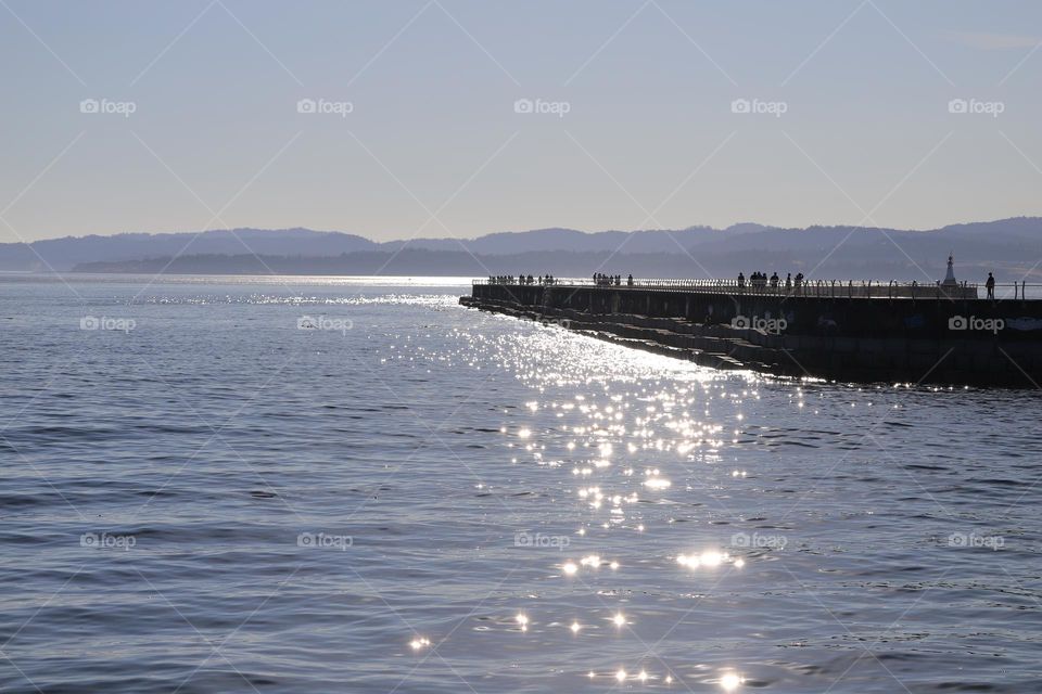 Sunshine in the ocean and people walking on breakwater 