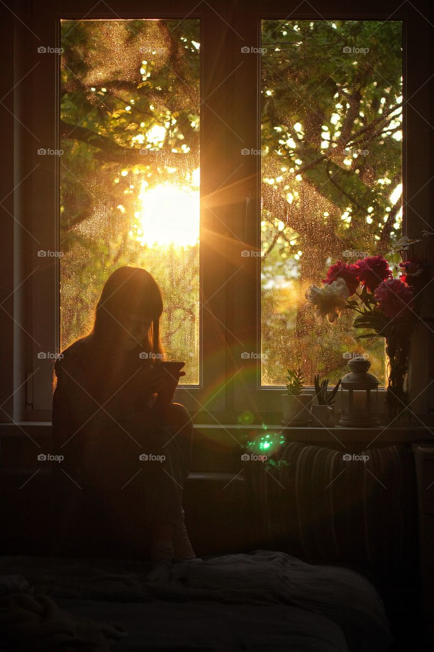 Little girl sitting by the window at sunset