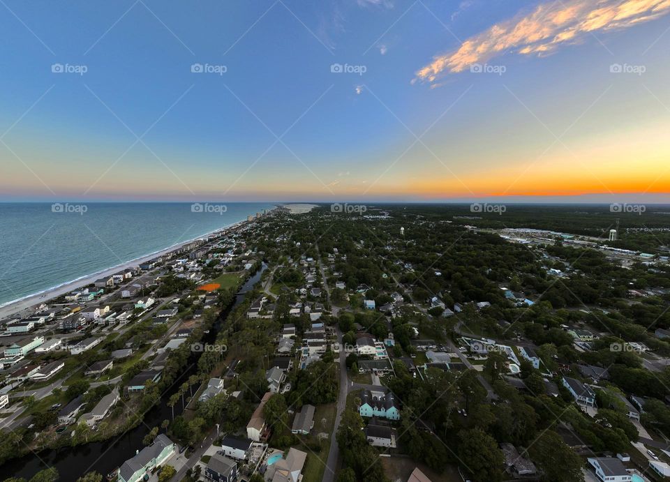 Vertical drone photo over surfside beach as the sun sets to the right and the ocean waves crash on the shore to the left, the beautiful colors of all the beach homes pop with brightness