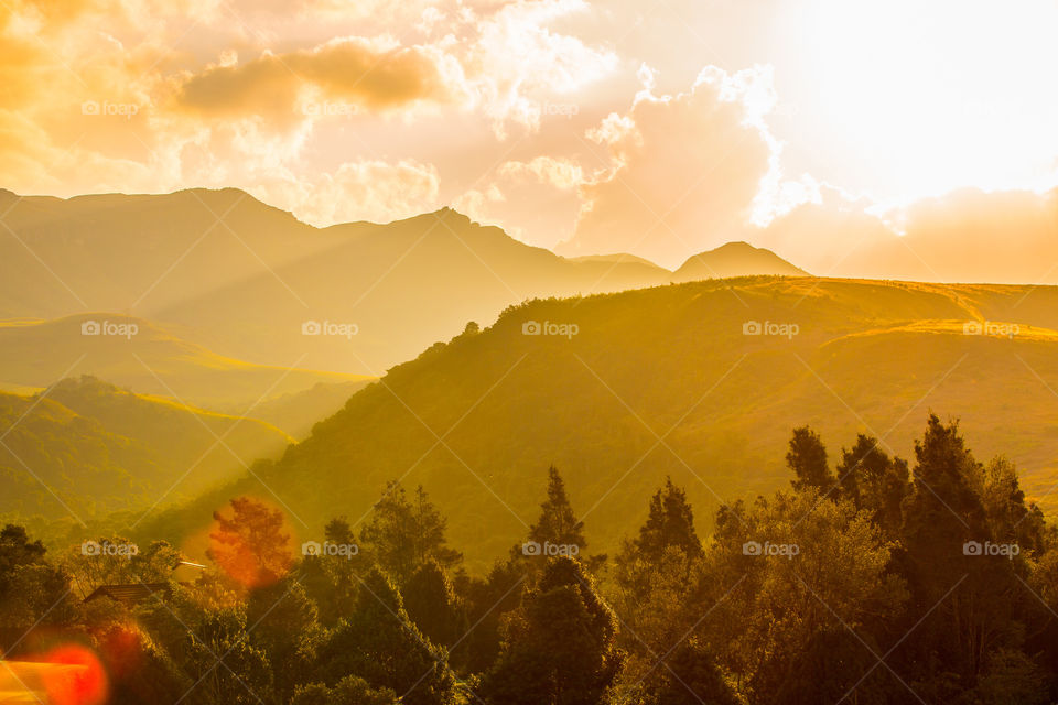 Sunset with clouds over the mountains with trees and hills. Golden hour as sun hits the mountains. Beautiful calm sunset in Africa