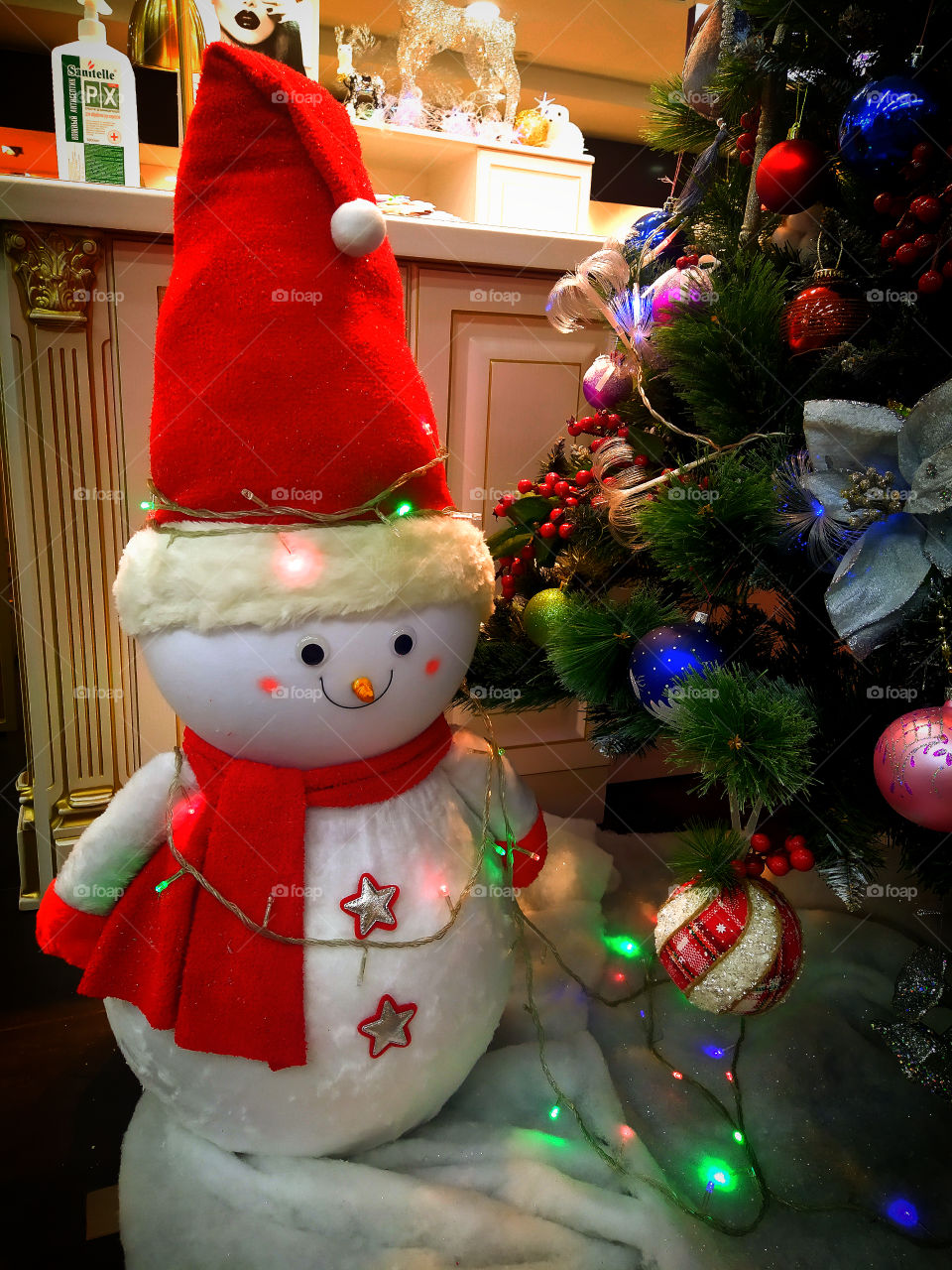 Decor.  Snowman in a red cap and a red scarf under the Christmas tree