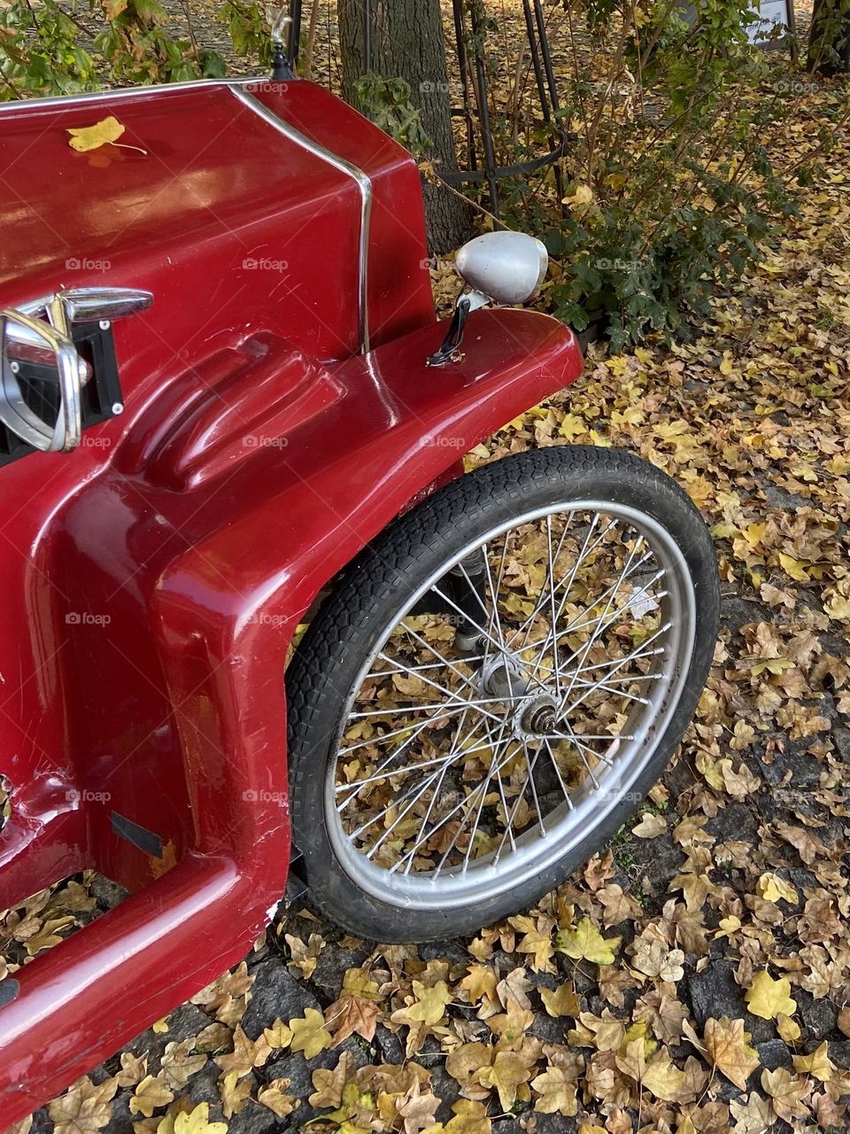 A classic old red car surrounded by fallen leaves on a a dirt road.