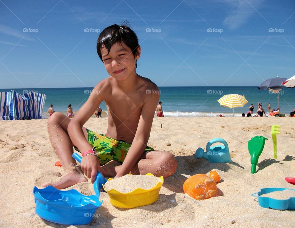 Young boy playing with his toys on the beach on a happy summer day
