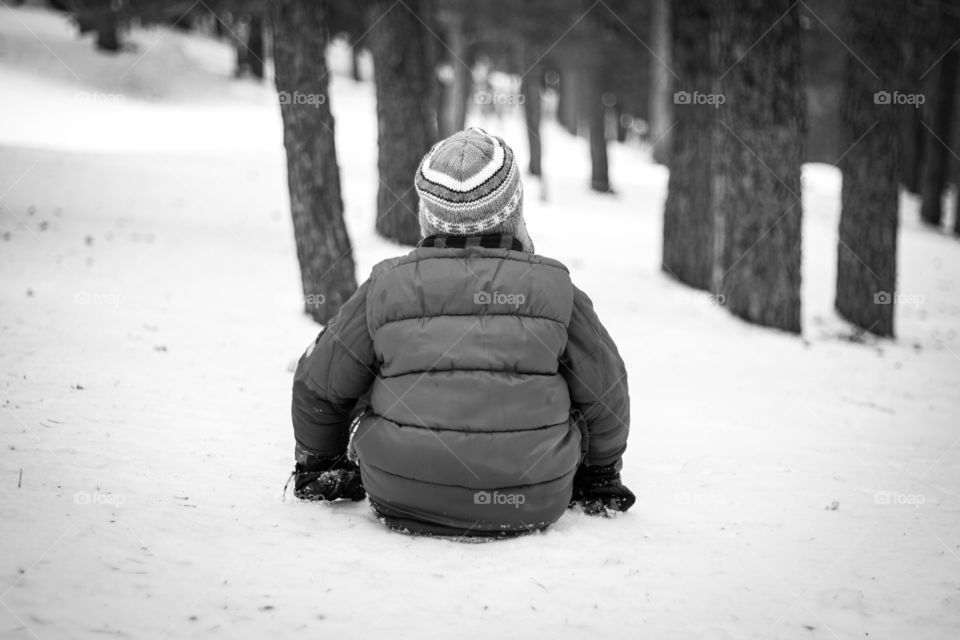Child sitting in the snow and looking to the forest.