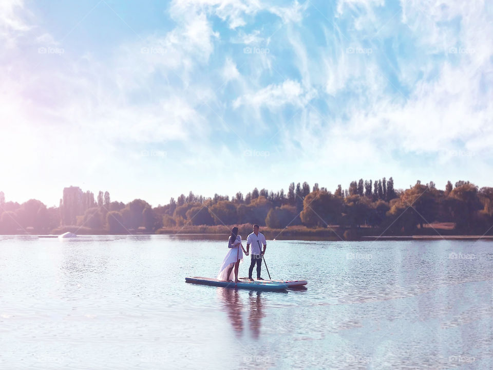 Couple in love holding hands and standing on the paddle board in the middle of the lake 
