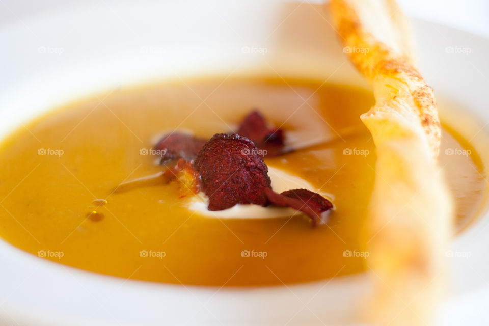 A bowl of warm soup with beet crisps and  bread twist