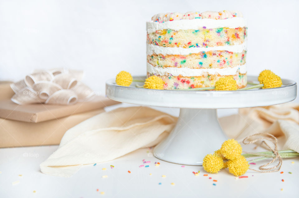 Bright image of a confetti birthday cake on a cake stand with wrapped gifts