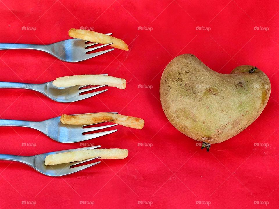 A heart-shaped potato with four metal forks next to it.  On each fork is a straw of french fries.  red background