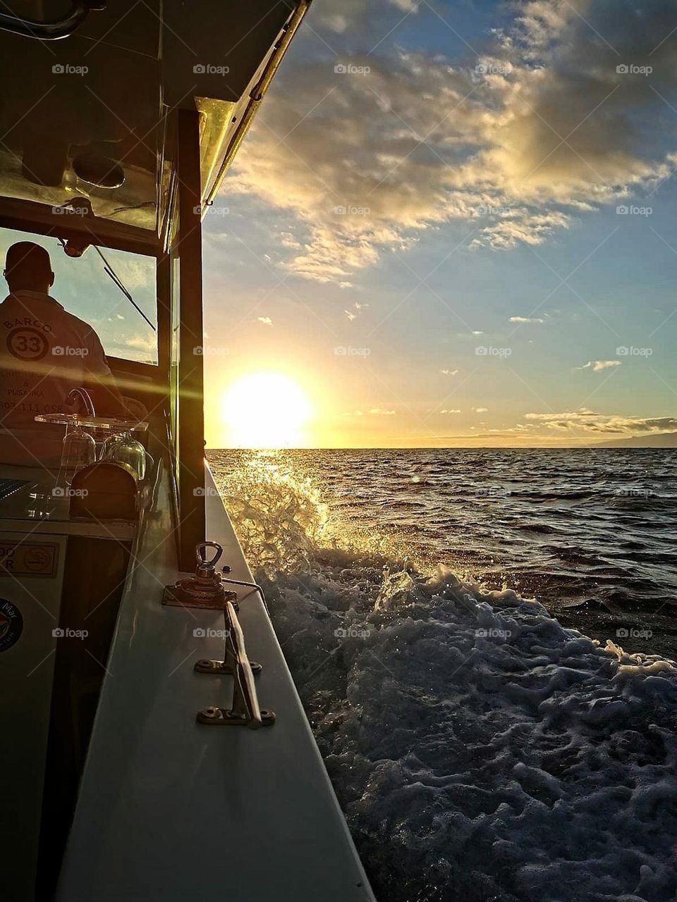 Clouds.Against the sunset.A yacht is sailing across the sea.A man sits in front of the controls.From the rapid movement of the yacht water foams.The sun is setting on the horizon.Clouds in the sky reflect the sunset,but have a silvery outline around