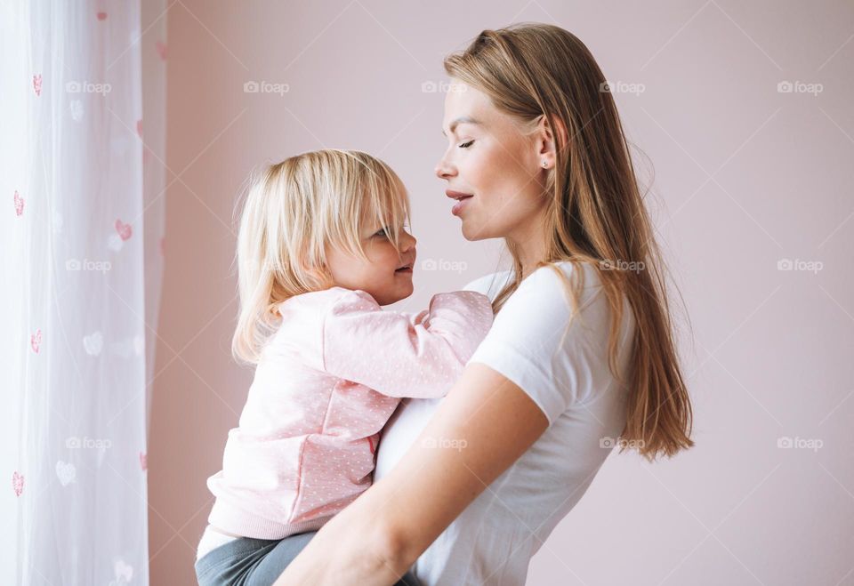 Portrait of young woman mother with baby girl daughter on hands at home