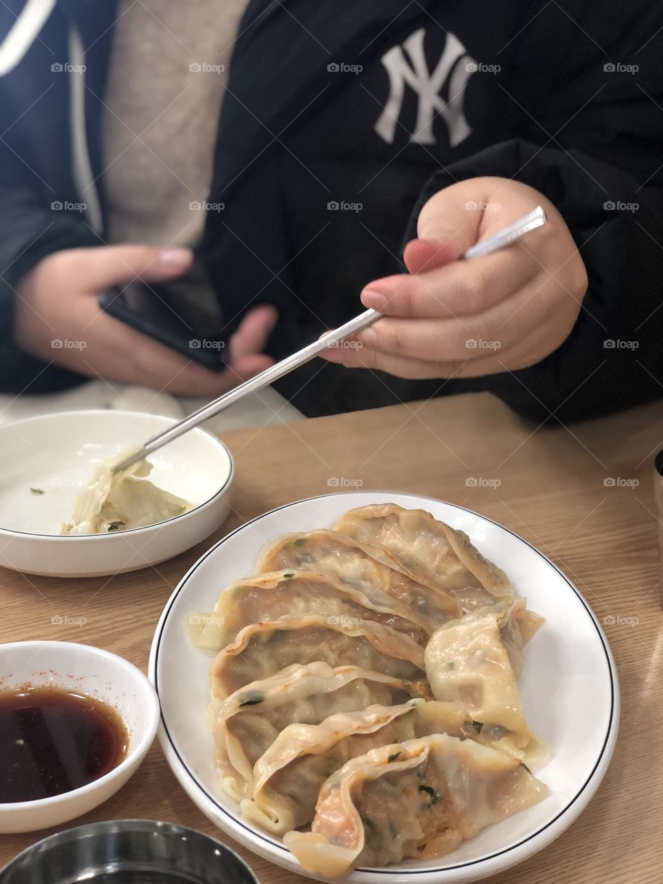 Hand holding phone and picking dumpling up with chopsticks 