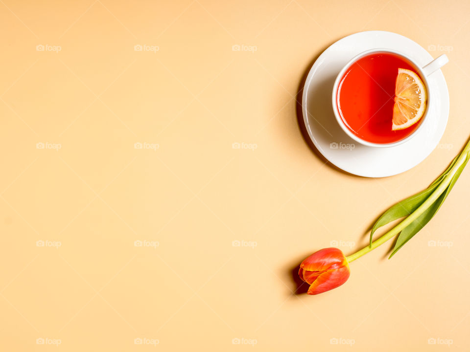 A cup of tea and a red tulip on a yellow background 