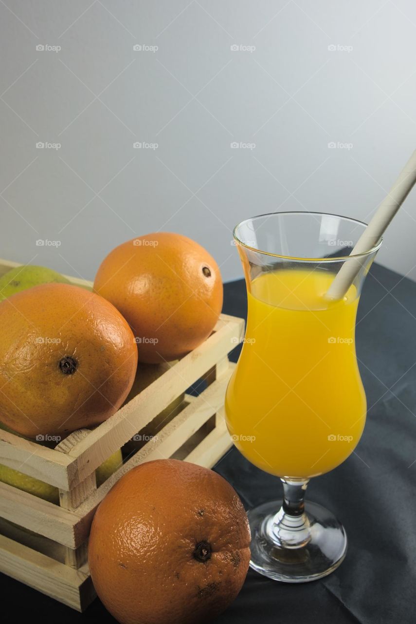 Oranges and glass tumbler with orange juice on black background