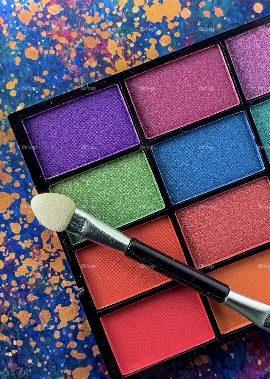 Make up palette in vibrant colours against a background of gold splattered colourful patterns