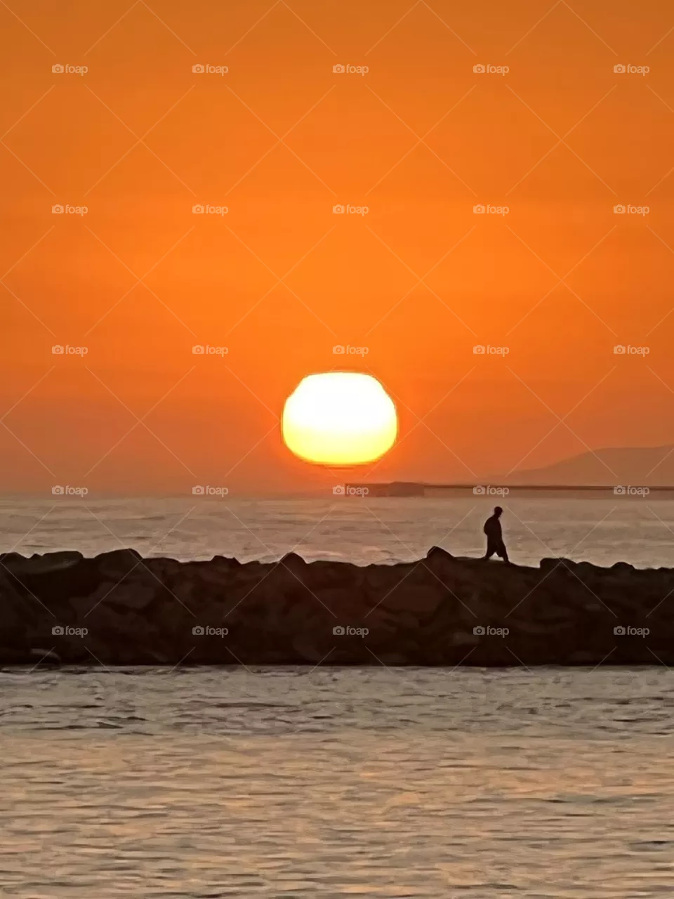 Beautiful sunset over the Newport Beach Jetty with a man walking in front of it